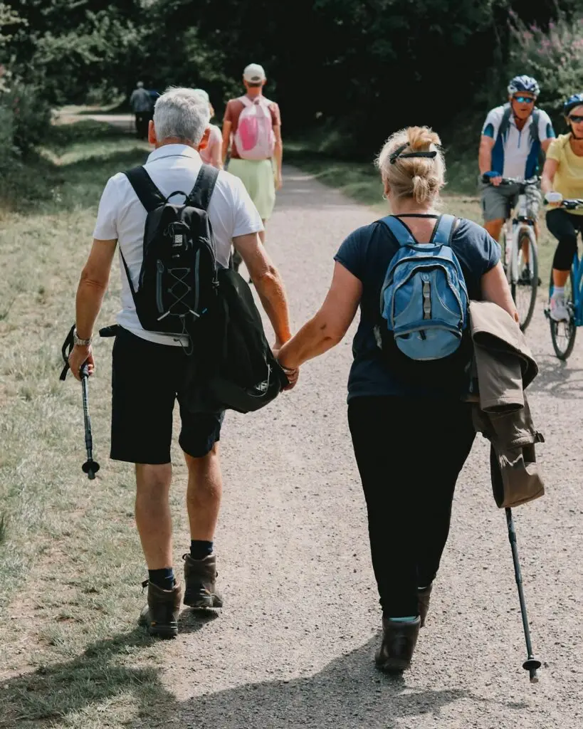 An older couple walking together on a park trail with hiking poles